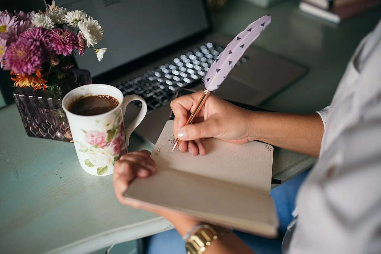 Notes being written beside a laptop with coffee on the desk